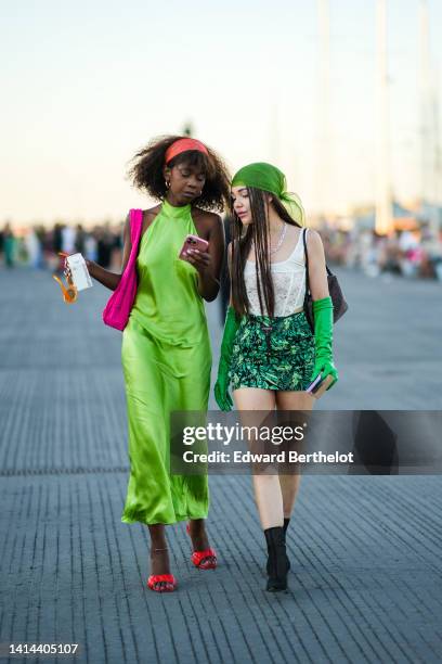 Guest wears a red large headband, gold earrings, a green halter-neck / sleeveless / long silk dress, a neon pink sponge shoulder bag, red quilted...