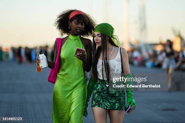 Guest wears a red large headband, gold earrings, a green halter-neck / sleeveless / long silk dress, a neon pink sponge shoulder bag, a guest wears a...