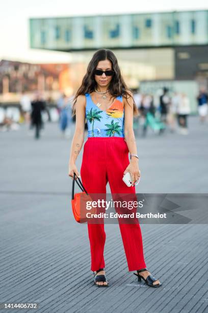 Guest wears black sunglasses, a white pearls necklace, gold shell and butterfly pendant necklaces, a multicolored landscape print pattern V-neck /...