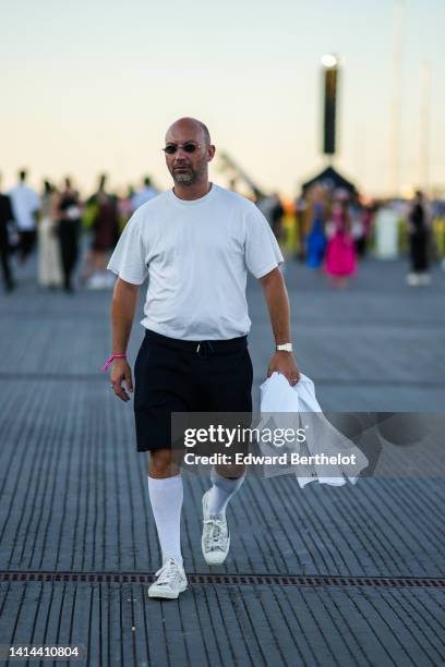 Guest wears black circle sunglasses, a white t-shirt, black suit pants, a white denim jacket, a silver watch, rings, white high waist socks, white...