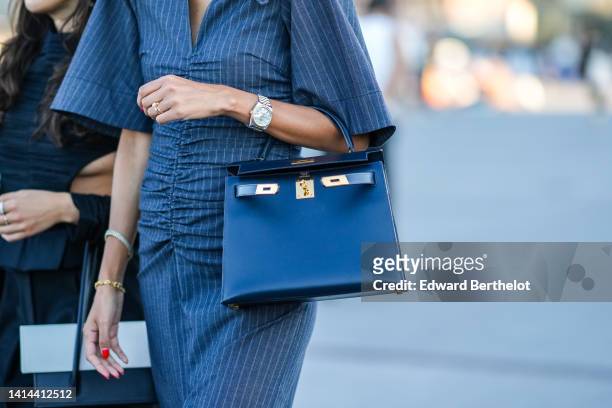 Guest wears a dark gray striped print pattern short sleeves / slit shirt long dress, a black shiny leather Kelly handbag from Hermes, a silver and...