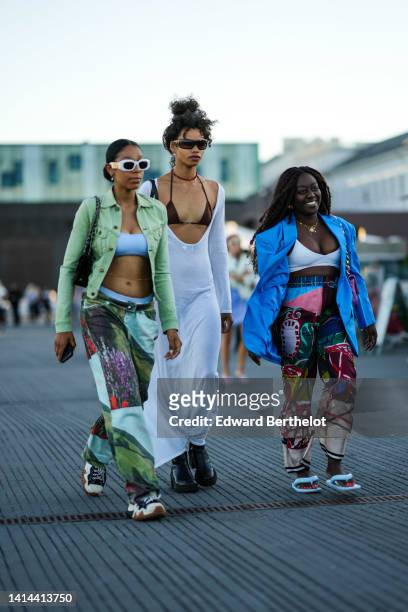 Guest wears white sunglasses, a white shoulder-off / cropped top, a green denim jacket, green / brown / black denim print pattern flared pants with...