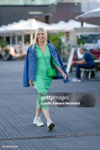 Guest wears a gold long chain pendant necklace, a green ribbed V-neck / long tube dress, a blue denim jacket, a neon green shiny leather braided...