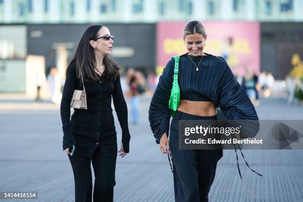 Guest wears black sunglasses, gold earrings, gold chain pendant necklaces, a black buttoned ribbed wool cardigan, matching black ribbed flared pants,...