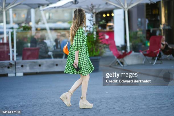 Guest wears sunglasses, a neon green and dark green checkered print pattern puffy long sleeves short dress, an orange shiny leather shoulder bag,...