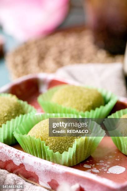 Close up of asian traditional rice dessert sweet green matcha mochi in pink ceramic dish on blue table. Spring pink flowers at background.