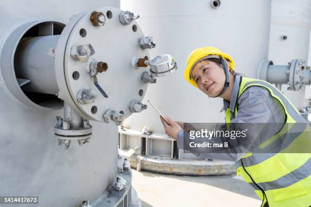 a female engineer works on a tablet computer at the construction site of a chemical plant - premium gasoline stock pictures, royalty-free photos & images