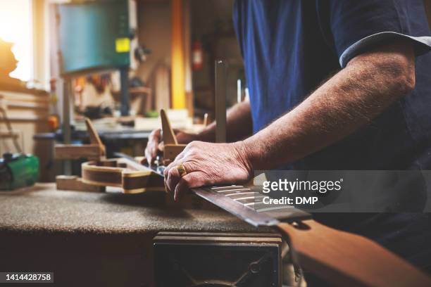 closeup of man hands repairing, fixing and building a guitar in luthiers service workshop. professional male standing, measuring and servicing music instrument on workbench in his garage. - instrumentenmaker stockfoto's en -beelden