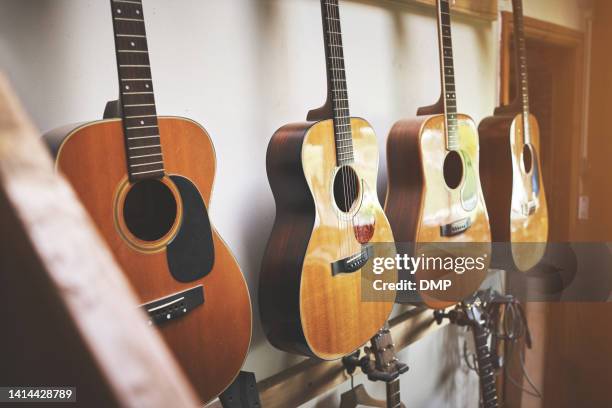 group of classic musical guitar instruments on display in a music shop. classical vintage acoustic guitars or  instruments made from art wood hanging on a rack in a new indoor local store. - gitaar stock pictures, royalty-free photos & images