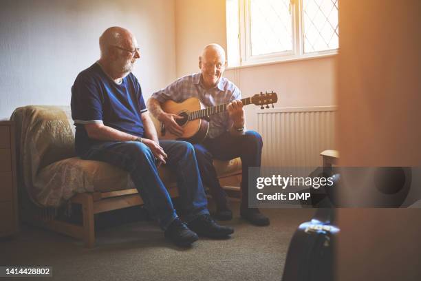 senior men having fun with a guitar, bonding while playing music together at home. retired musicians smiling, enjoying rhyme of sound and bonding. friends singing and spending time indoors - moment friends men european stockfoto's en -beelden