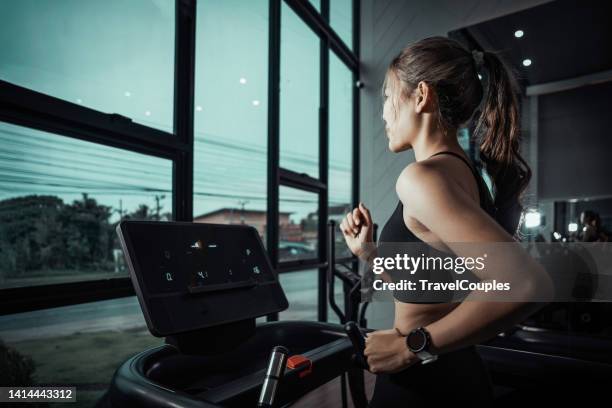 woman running in a gym on a treadmill concept for exercising. fitness and healthy lifestyle. girl running on the treadmill and listening to music at the gym - トレッドミル　女性 ストックフォトと画像