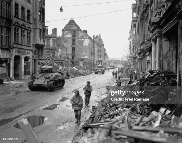 Sherman medium tanks and infantry soldiers of the 3rd Armoured Division, VII Corps, United States First Army advance through the battle damaged...