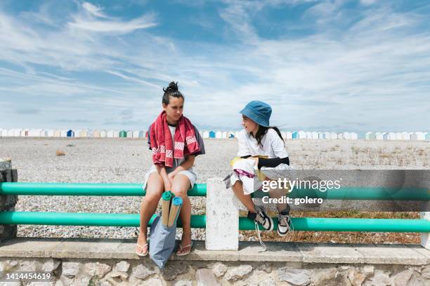 teenager-mädchen sitzt mit kleiner schwester auf balustrade am kiesstrand in frankreich - normandy stock-fotos und bilder