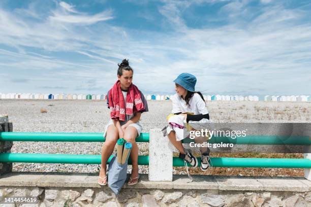 teenage girl sitting with little sister on balustrade at pebble beach in france - hauts de france 個照片及圖片檔