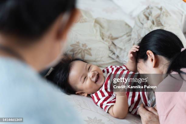 little cute asian baby boy having fun and playing with his mother while lying on bed. - belly kissing stock pictures, royalty-free photos & images