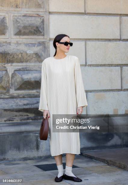 Guest is seen wearing creme white long dress, brown bag, white socks, black shoes outside Helmstedt during Copenhagen Fashion Week Spring/Summer 2023...