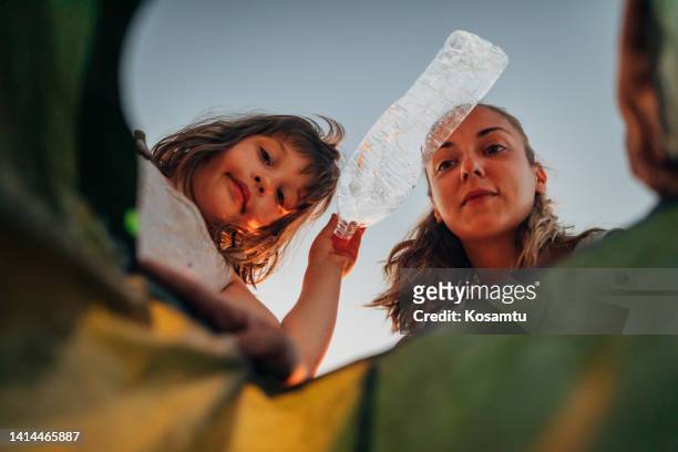 a woman and a little girl throw plastic bottles into a plastic bag - glasbak stockfoto's en -beelden
