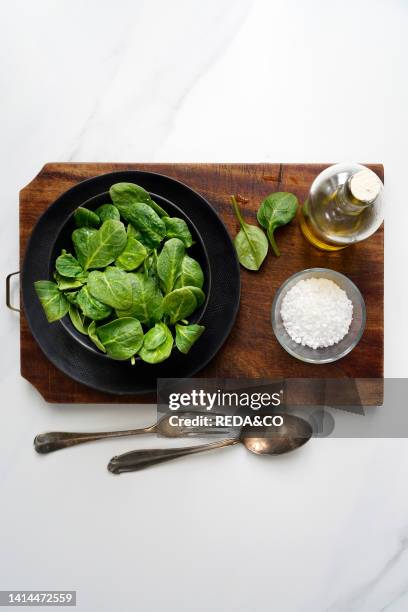 Fresh baby spinach in a black bowl. Silver cutlery on an old wooden cutting board.