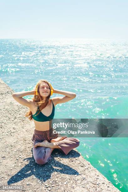 young woman enjoys a walk by the sea and listens to music on a sunny day. hair in the wind. - beach yoga stock-fotos und bilder