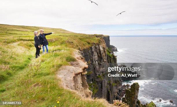 zwei touristinnen, die am rande der klippe stehen und den meerblick betrachten - ireland vacation stock-fotos und bilder