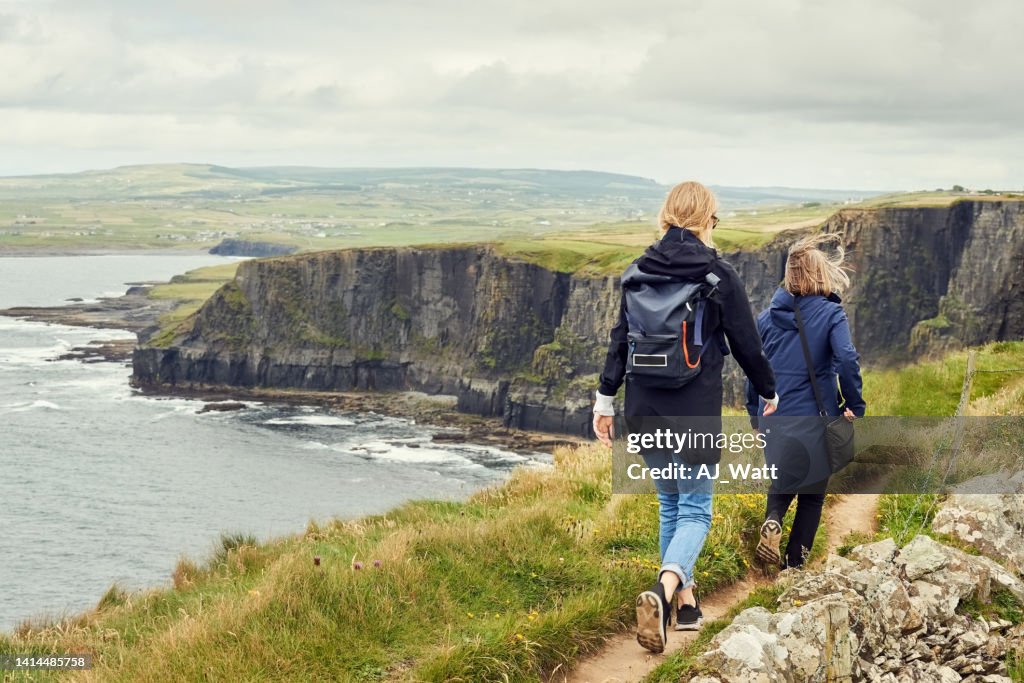 Two women friends walking on the trail on the cliff