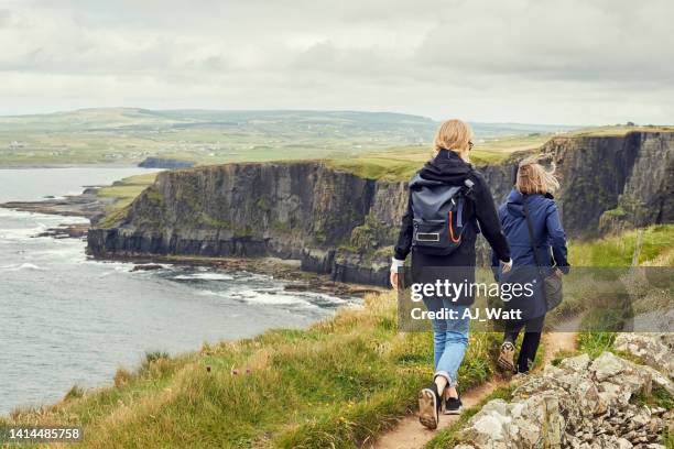 two women friends walking on the trail on the cliff - irisch stock pictures, royalty-free photos & images