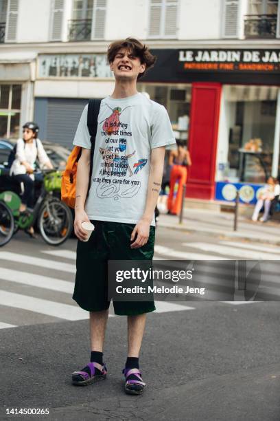 Model, designer, and artist Audi Bizar wears a white illustrated Audi Bizar shirt with text, knee-length green shorts, black socks, and purple...