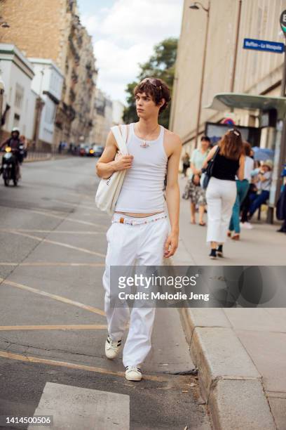 Model Jack Blanco wears a white fitted sleeveless tank top, white pants, white Adidas sneakers, and a beaded 90's Y2K style belt at the Amiri show at...