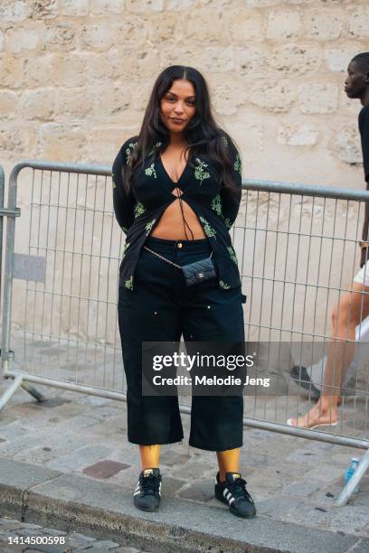 Model Paloma Elsesser wears a front tie black cardigan with beads, miniature waist belt bag Chanel purse, black capri pants, and black and white...