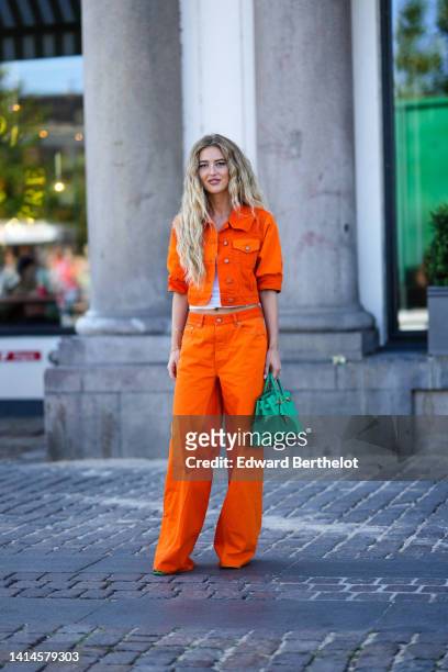 Emilli Sindlev wears earrings, a neon orange denim short sleeves / cropped shirt from Ganni, matching neon green denim wide legs pants from Ganni, a...