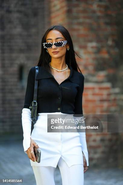 Nephtys Laurent wears black and white checkered print pattern sunglasses, silver necklaces, silver earrings, a half black ribbed and half white...
