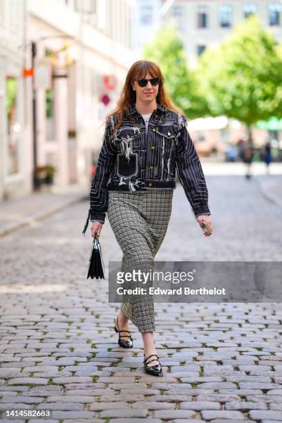 Erin Fitzpatrick wears black sunglasses, a white t-shirt, a white and red pearls necklace, a navy blue with embroidered / ripped white seams denim...