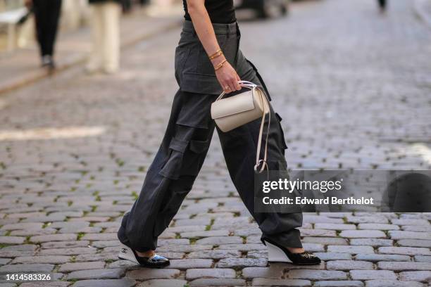 Annabel Rosendahl wears a black turtleneck / shoulder-off / sleeveless / body top, dark gray large cargo pants, a gold watch, gold rings, gold Love...