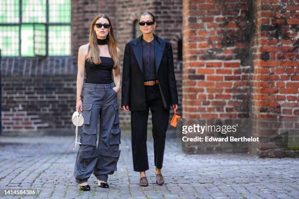 Annabel Rosendahl wears black sunglasses, gold earrings, a black turtleneck / shoulder-off / sleeveless / body top, dark gray large cargo pants, a...