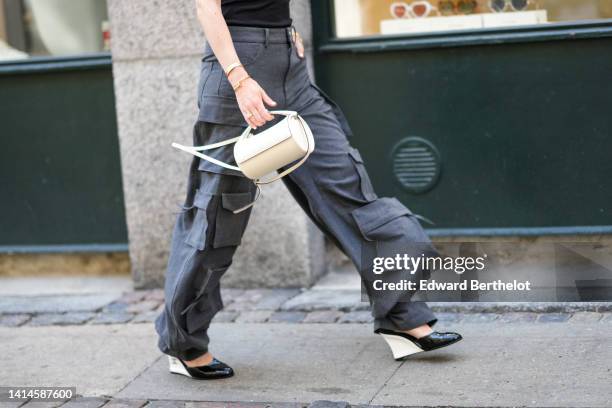 Annabel Rosendahl wears a black turtleneck / shoulder-off / sleeveless / body top, dark gray large cargo pants, a gold watch, gold rings, gold Love...