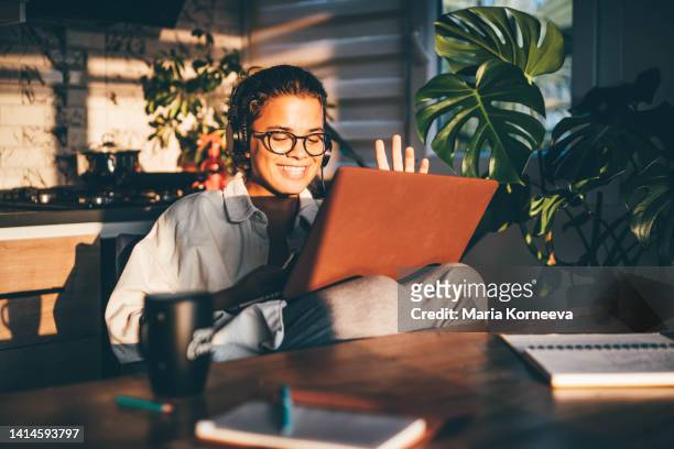 young smiling woman with headphones having video call at home. - conversation sunset stock-fotos und bilder
