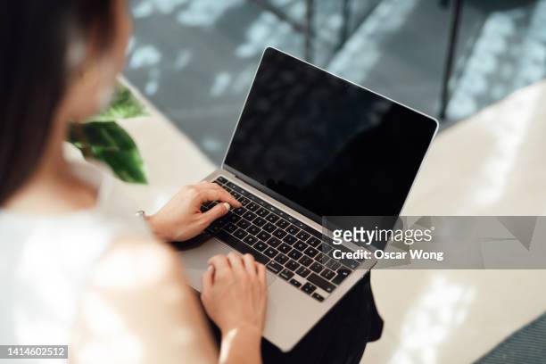 over the shoulder view of young woman using laptop - laptop back stock pictures, royalty-free photos & images