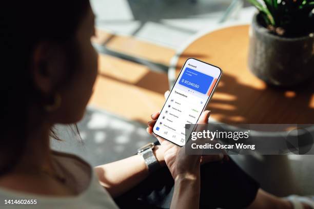 over the shoulder view of young woman managing personal bank account with smart phone at home - vista por la espalda fotografías e imágenes de stock