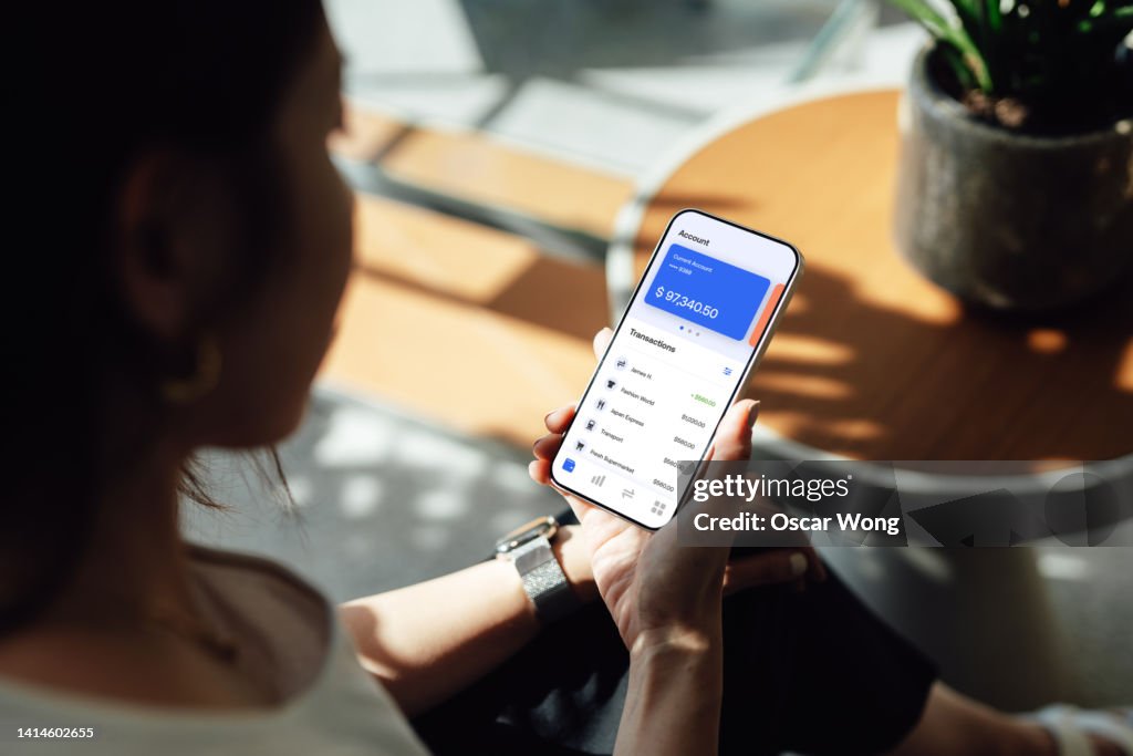 Over the shoulder view of young woman managing personal bank account with smart phone at home