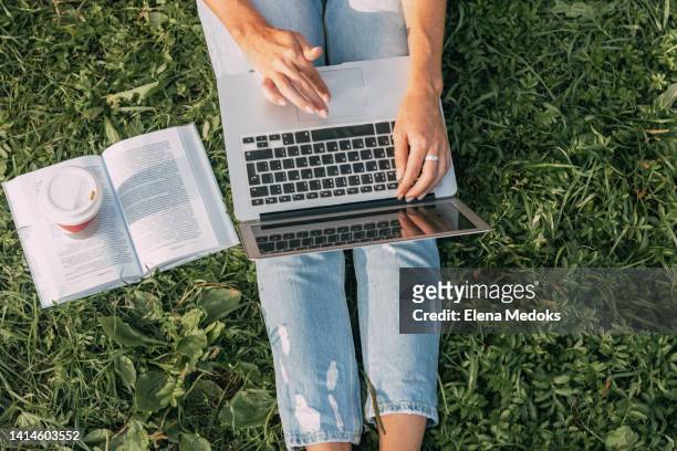 top view of a laptop on the legs of a girl sitting in the park on the grass. freelancer at work. girl communicates online and watches webinars - lernen stock-fotos und bilder