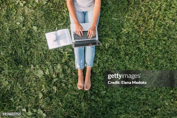 top view of a laptop on the legs of a girl sitting in the park on the grass. freelancer at work. girl communicates online and watches webinars - mujer leyendo libro en el parque fotografías e imágenes de stock