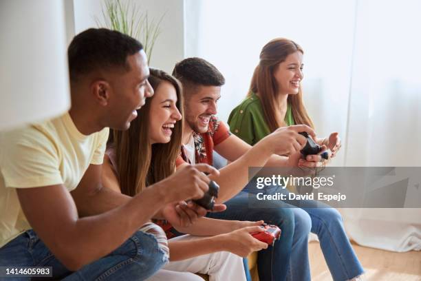 happy friends enjoying playing video games while sitting on a sofa at home. - game four stockfoto's en -beelden