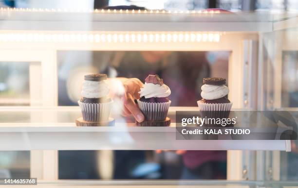 hands putting chocolate cupcakes on glass cabinet, front view of hands putting chocolate cupcakes on glass cabinet - boulangerie vitrine stock pictures, royalty-free photos & images