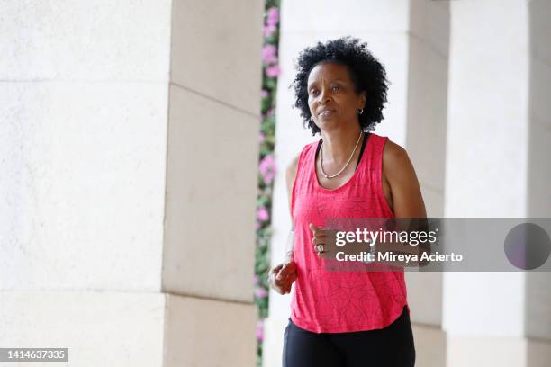 a mature african american woman with curly hair, runs through an outdoor passage during the day while wearing a pink colored tank top and black biker shorts. - running shorts foto e immagini stock