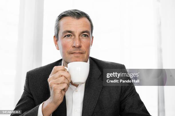 portrait of an elegant, middle-aged businessman having a cup of coffee while being a bit worried - great recession stock pictures, royalty-free photos & images