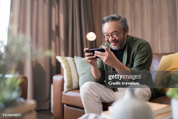 asian adult mature male online gaming addiction,exited fun asian man laugh smile hand playing esport digital game virtual online smartphone compettition with online friend around the world closeup shot at home - mobile game stock pictures, royalty-free photos & images