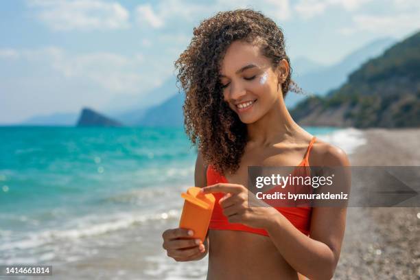 smiling woman is applying suntan lotion on her face - tanned body stock pictures, royalty-free photos & images