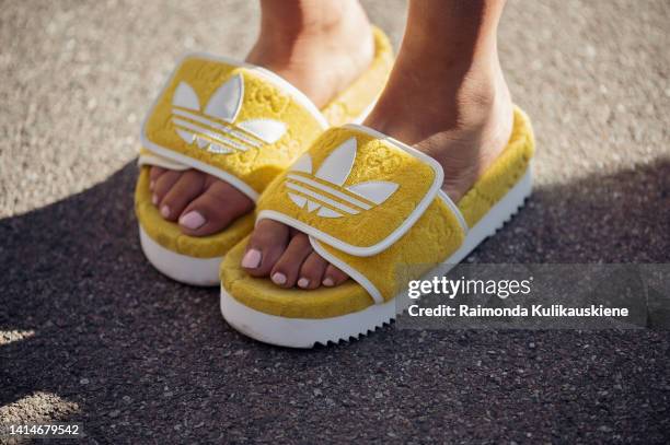 Selma Kaci wearing yellow and green dress, yellow mini bag, yellow Adidas slippers, black sunglasses and headphones posing outside Henrik Vibskov...