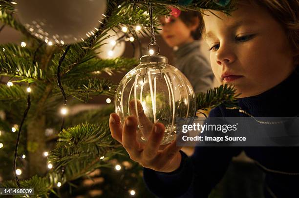 boy decorating christmas tree with baubles at home - mensen op de achtergrond stockfoto's en -beelden