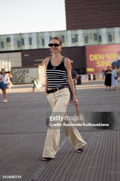 Pernille Teisbaek wearing beige pants, black and white Chanel top and black sunglasses posing outside Ganni during Copenhagen Fashion Week...
